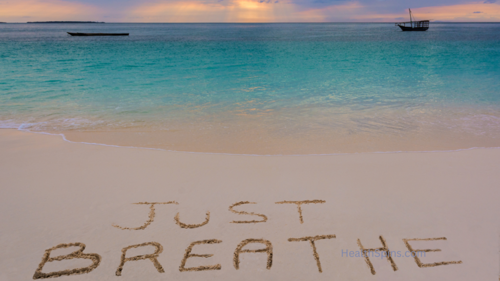 A tranquil beach scene with "JUST BREATHE" written in the sand. The turquoise ocean waves gently lap the shore, and a boat floats in the distance under a colorful sky.